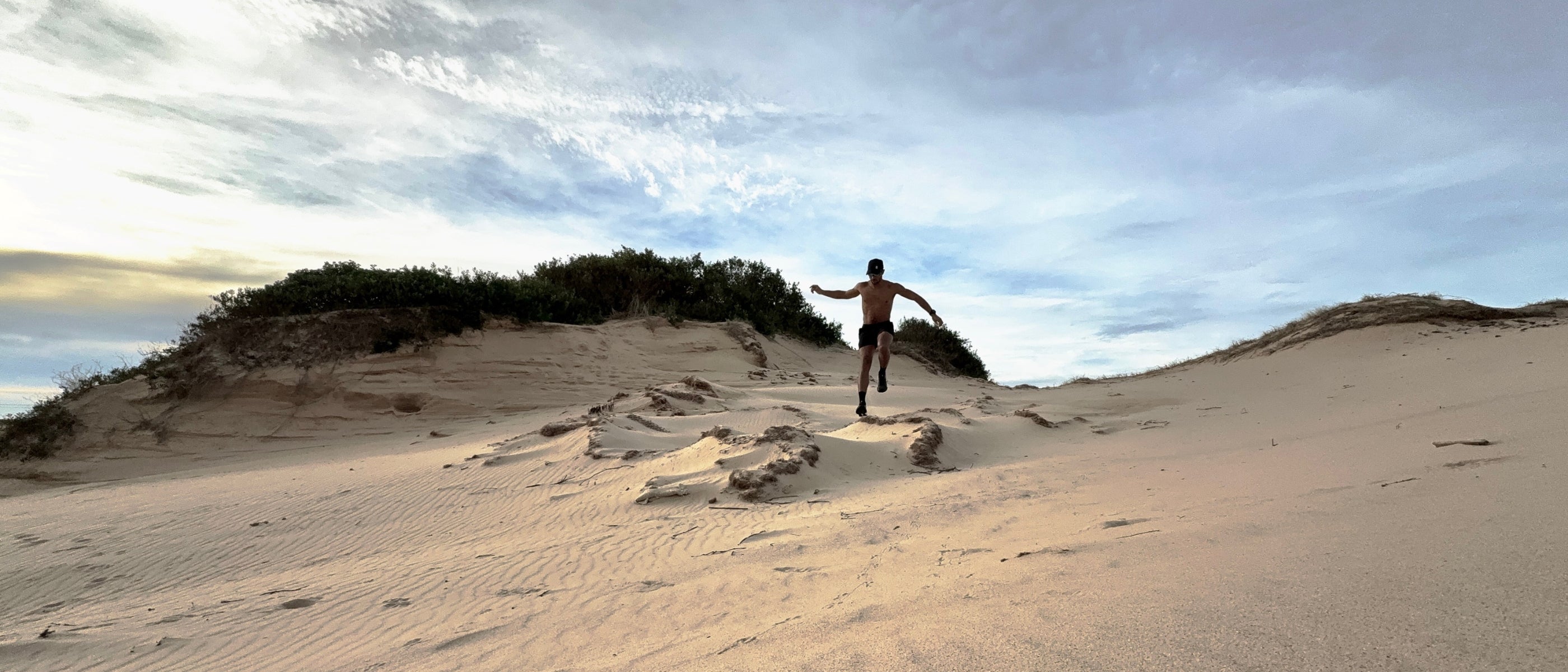 Athlete running across coastal sand dunes wearing ruhn performance trunks